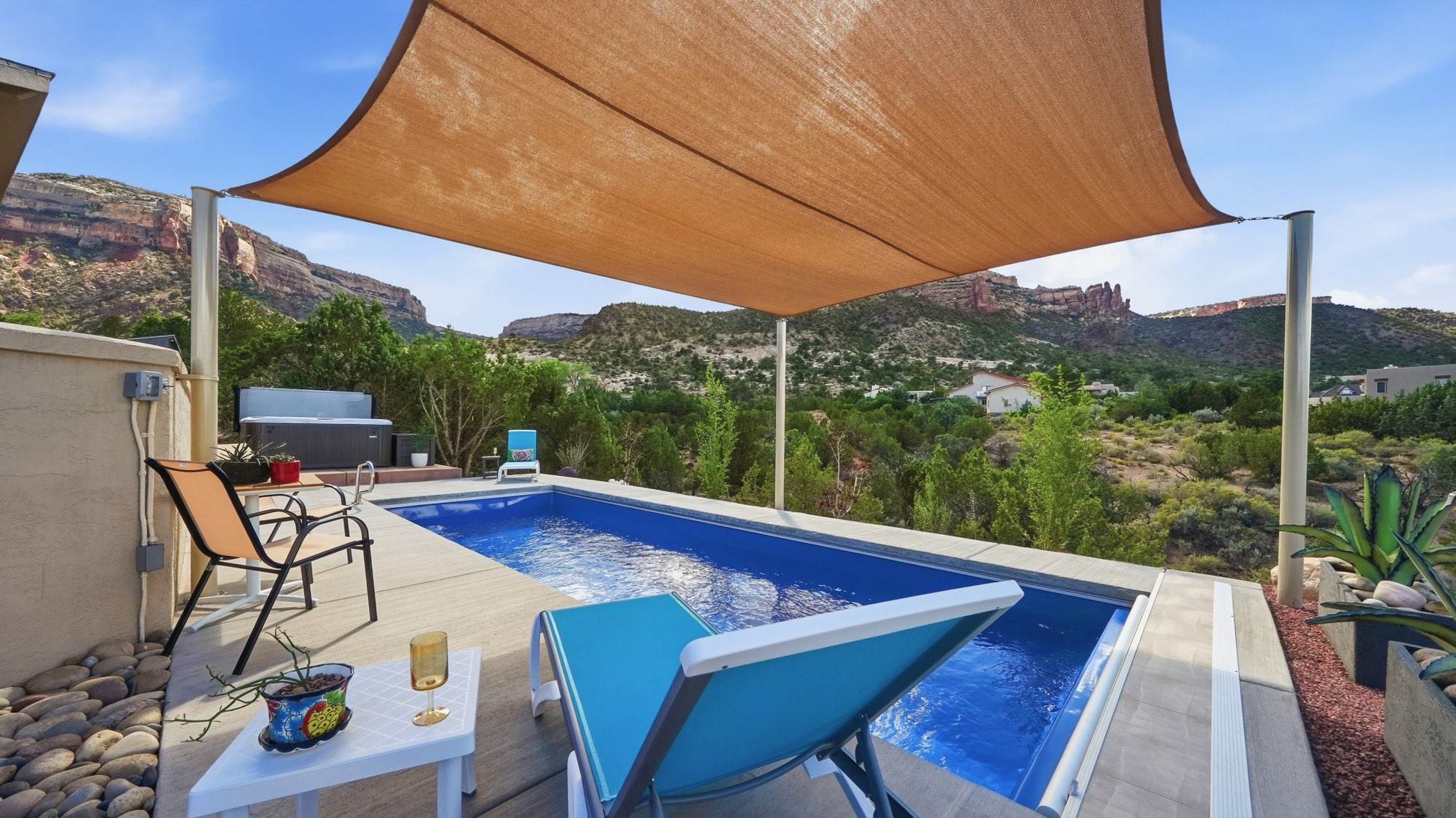 A tan canvas shade sail stretched over a backyard pool in Grand Junction, Colorado, with the red cliffs of the Colorado National Monument behind it