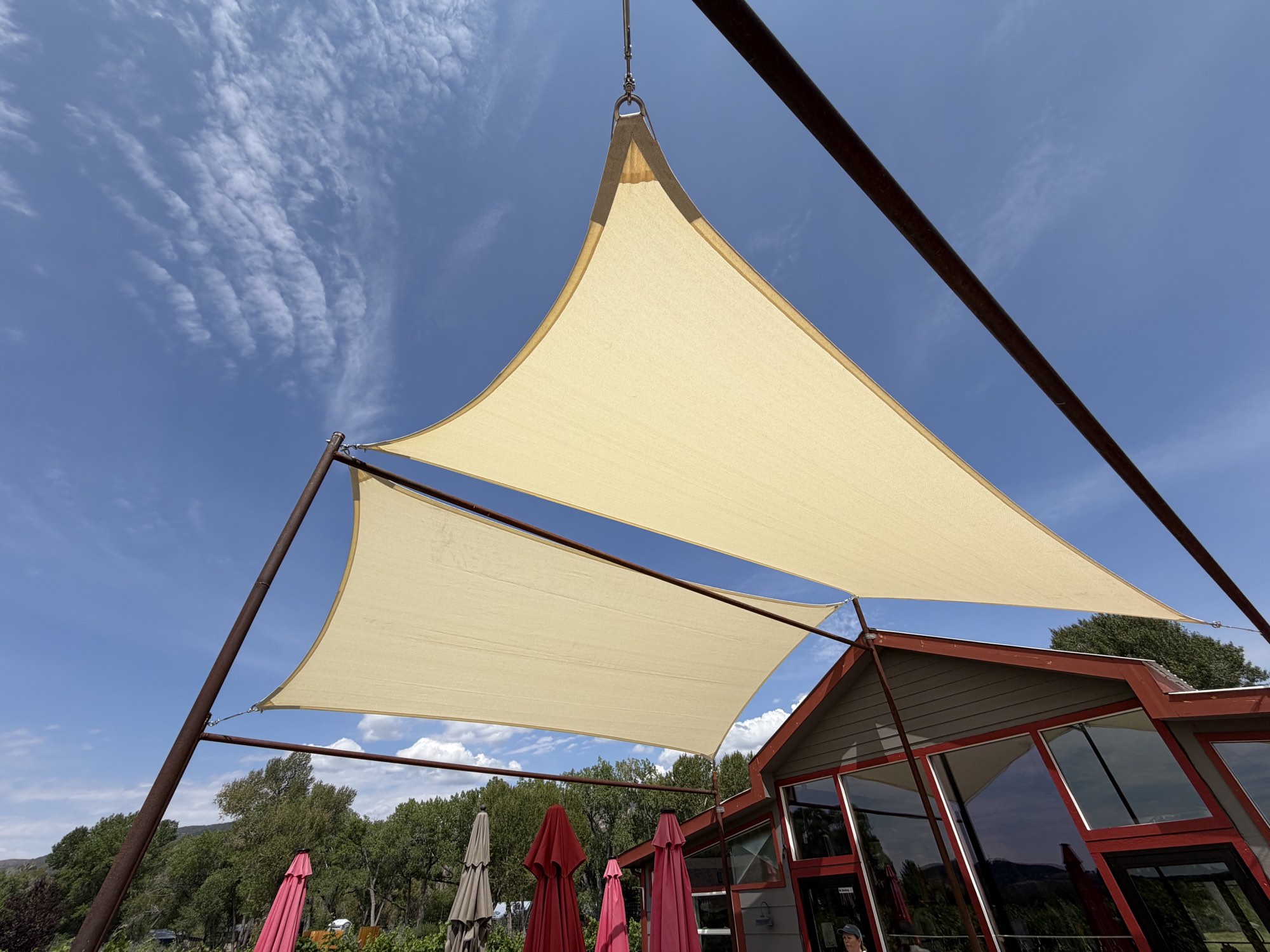 Two cream shade sails against a blue sky above the Painted Vineyard tasting patio in Paonia