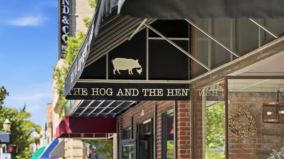 A black storefront awning printed with The Hog and the Hen logo over a brick shopfront
