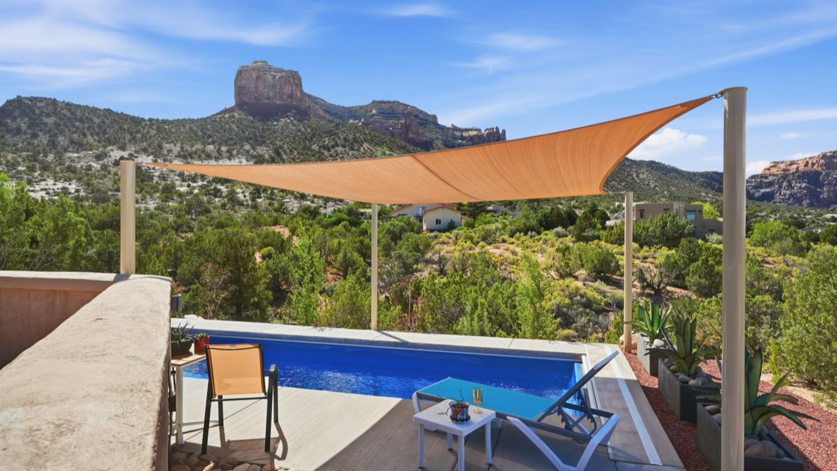 A tan shade sail over a backyard pool deck with the Colorado National Monument in the background